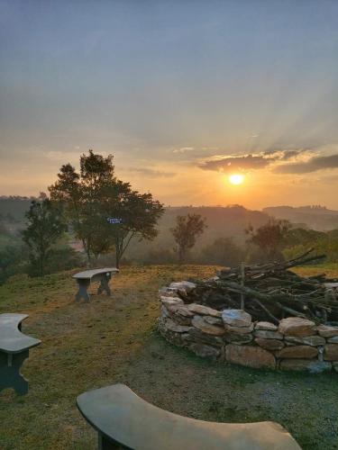 a sunset in a field with a stone wall and benches at Hotel Morro De Santo Agostinho in Serra Negra