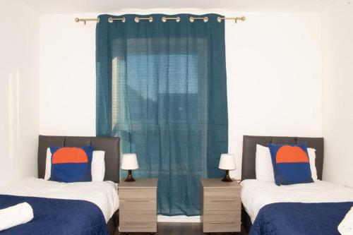 ein Schlafzimmer mit 2 Betten und einem blauen Vorhang in der Unterkunft TMS Beautiful 2 Bedroom Apartment!Ensuite!Dovestone Lakeside in West Thurrock