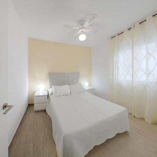 a white bedroom with a bed and a ceiling fan at Apartamento Murillo in Barbate