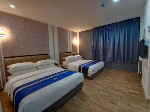 two beds in a hotel room with blue curtains at GOOD 9 HOTEL - Cahaya Kota Puteri in Pasir Gudang