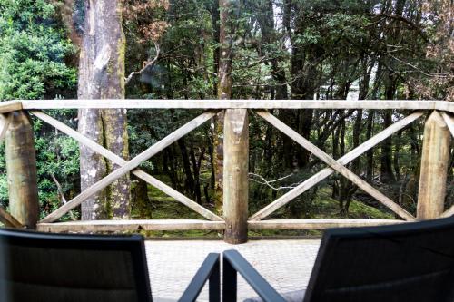 a wooden fence with two chairs in front of a forest at Peppers Cradle Mountain Lodge in Cradle Mountain
