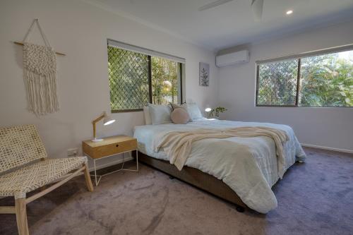 a bedroom with a bed and a chair and two windows at Hidden Oasis - Peregian Beach in Peregian Beach