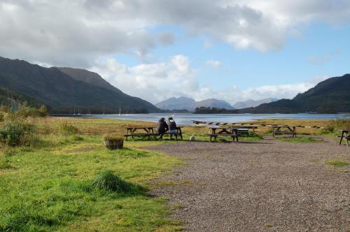 two people sitting on picnic tables next to a lake at Duart Cottage in Glencoe