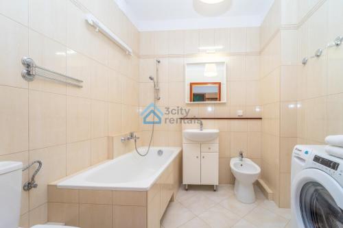 a bathroom with a tub and a toilet and a washing machine at Botanika Deluxe Apartment Sopot in Sopot