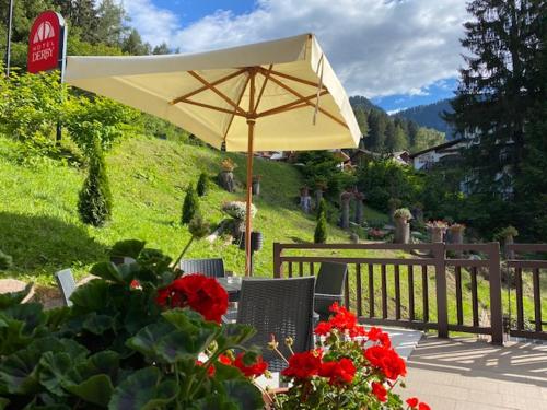 une table avec un parasol et quelques fleurs rouges dans l'établissement Hotel Derby, à Folgarida