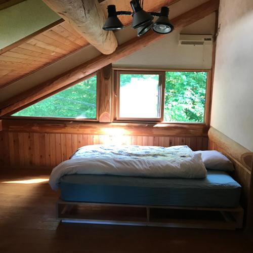 a bed in a room with two windows at NaGano-log house in Chino