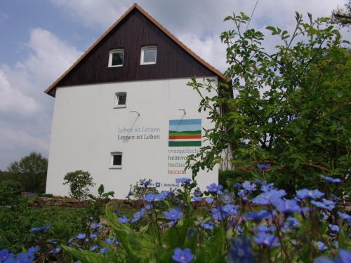 a white building with a black roof and blue flowers at Denkhaus Loccum in Rehburg-Loccum