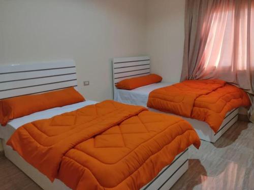 two beds in a room with orange sheets at Ramco For Furnished Apartments And Accommodation Compound Leila in Cairo