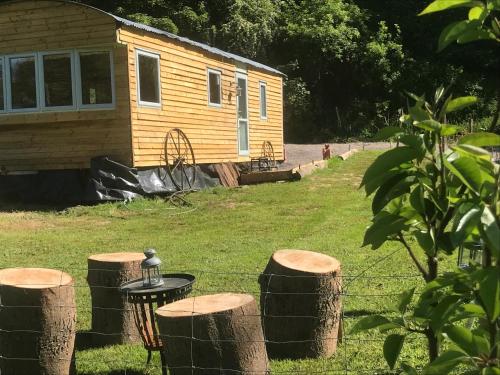 a cabin with a table and some logs in the grass at Shepherds Huts Ham Hill, 2 double beds, Bathroom, Lounge, Diner, Kitchen, LOVE dogs & Cats Looking out to lake and by Ham Hill Country Park plus parking for large vehicles available also great deals on workers long term This is the place to relax and BBQ in Yeovil
