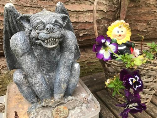 a statue of a gargoyle sitting on a table with flowers at Shepherds Huts Ham Hill, 2 double beds, Bathroom, Lounge, Diner, Kitchen, LOVE dogs & Cats Looking out to lake and by Ham Hill Country Park plus parking for large vehicles available also great deals on workers long term This is the place to relax and BBQ in Yeovil