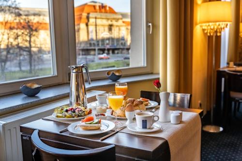 a table with breakfast foods and drinks and a window at Royal International Leipzig in Leipzig