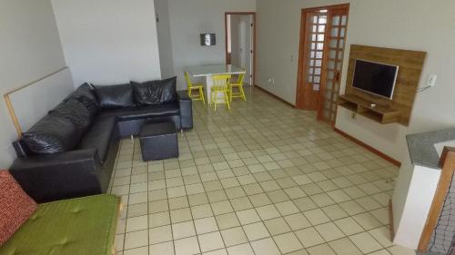 sala de estar con sofá de cuero negro y TV en Cobertura Duplex Virtudes, en Guarapari