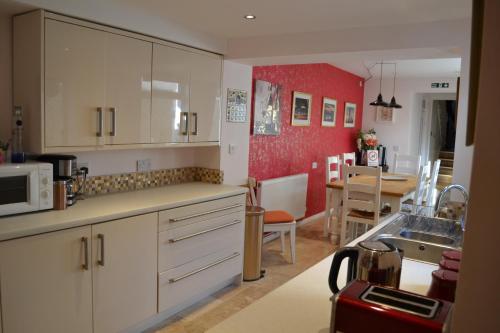 a kitchen with white cabinets and a red wall at Decimus in St. Leonards