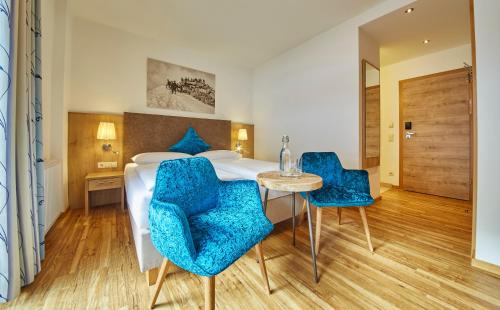 a hotel room with a bed with blue chairs and a table at Johanneshof - Dein MOUNTAIN Wohlfühlhotel in Saalbach Hinterglemm