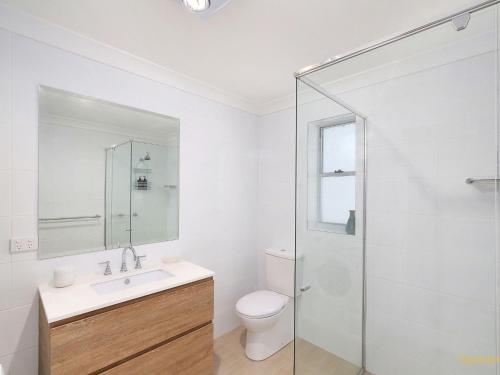 a white bathroom with a toilet and a glass shower at Seaside Symphony, Sleep and Wake to Ocean Waves in Wamberal