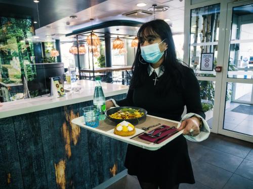 a woman wearing a mask holding a tray of food at ibis budget Bordeaux Aéroport in Mérignac