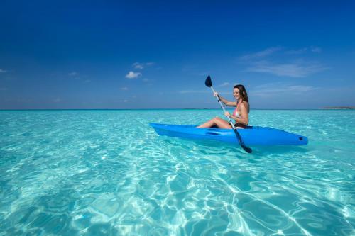 a woman is sitting on a boogie board in the ocean at Constance Moofushi Maldives - All Inclusive in Himandhoo 