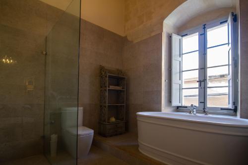a bathroom with a tub and a toilet and a window at Palazzino Birgu Host Family Bed and Breakfast in Vittoriosa