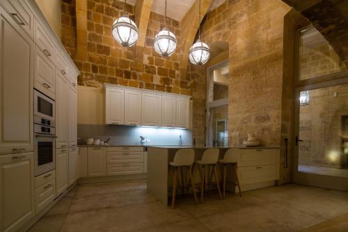 a kitchen with white cabinets and a stone wall at Palazzino Birgu Host Family Bed and Breakfast in Vittoriosa