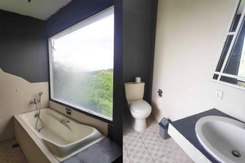 uma casa de banho com uma banheira, um WC e uma janela. em Pecatu GuestHouse em Uluwatu
