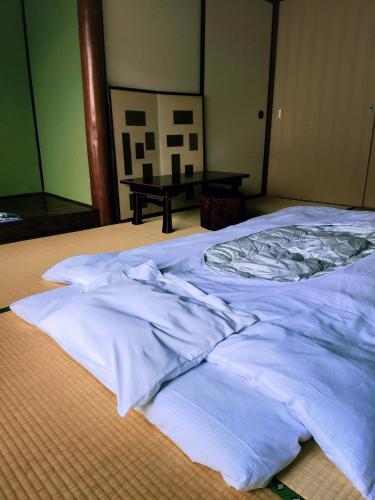 a bed with white sheets on top of it at Guesthouse Sakichi in Beppu