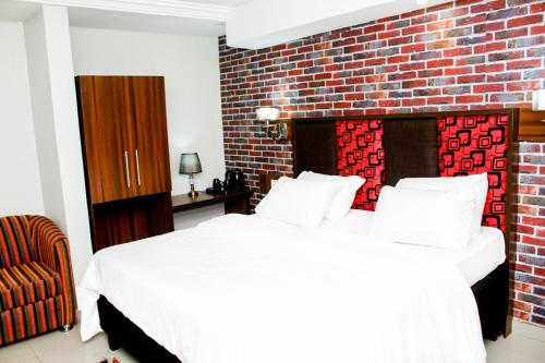 a bedroom with a white bed and a brick wall at Shamrockmanor(TheResidence) in Benin City