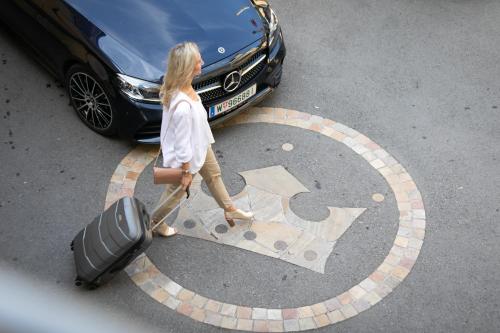 a woman walking with a suitcase in front of a car at Stadthotel zur goldenen Krone in Weiz