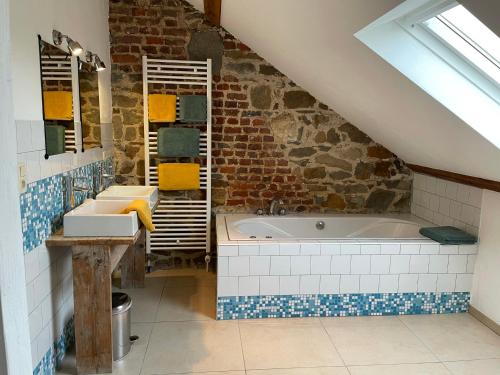 een badkamer op zolder met een bad en een stenen muur bij La Bushaye in Aubel