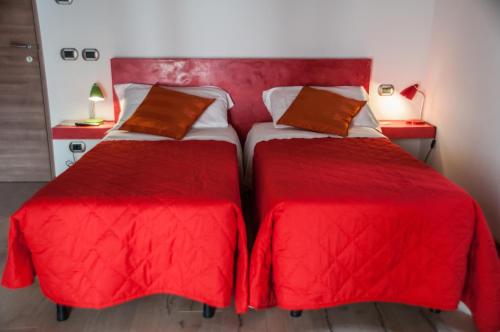 2 camas en una habitación con sábanas y almohadas rojas en B&B Santa Lucia, en Bérgamo