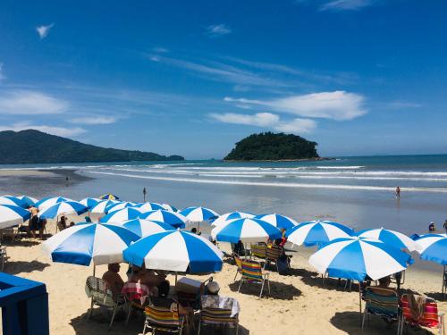 a group of people sitting under blue and white umbrellas on a beach at Kaliman Pousada in Ubatuba