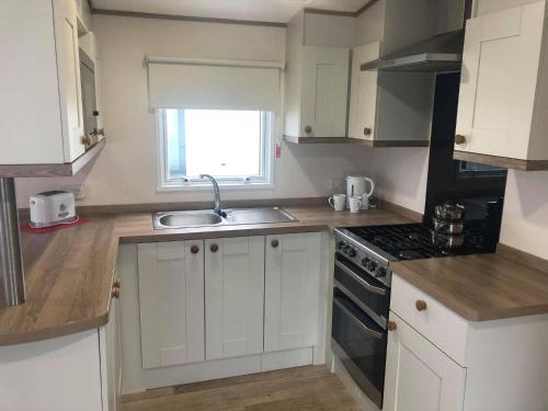 a kitchen with white cabinets and a sink and a window at Oak Prestige Holiday Home in Chapel Saint Leonards
