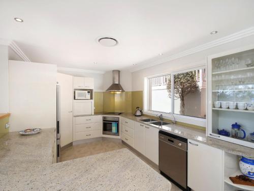 a large kitchen with white cabinets and a window at Enjoy Spectacular Oceanviews with BBQ & Airy Space in Terrigal
