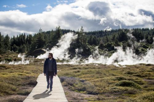 a man walking on a boardwalk with geysers in the background at Alpine Lake Motel in Taupo
