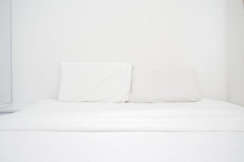 a white bed with a pillow on top of it at Comfy 2BR Apartment at Parkland Avenue By Travelio in Babakan