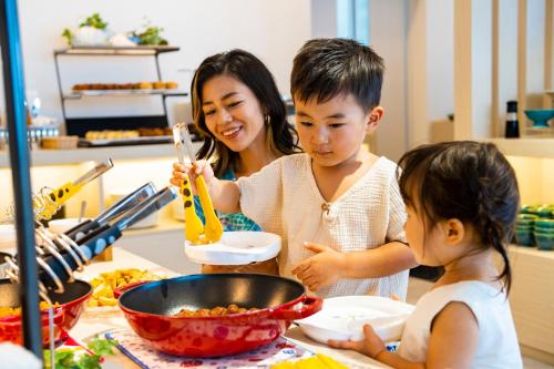 a woman and two children standing in a kitchen preparing food at Hotel Torifito Miyakojima Resort in Miyako Island