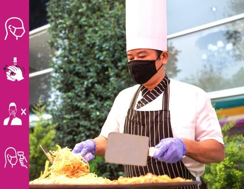 a man wearing a mask and apron preparing food at Hotel Royal Orchid Bangalore in Bengaluru