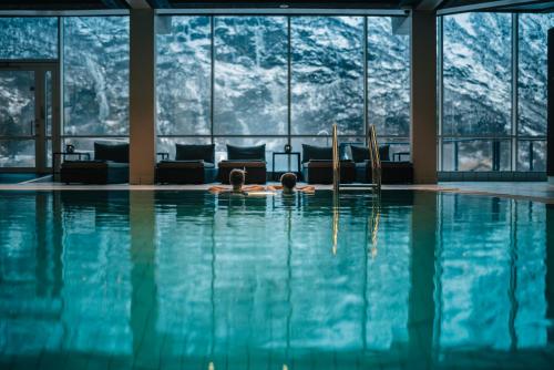 a woman laying in a swimming pool with a view of mountains at Hotel Union Geiranger Bad & Spa in Geiranger