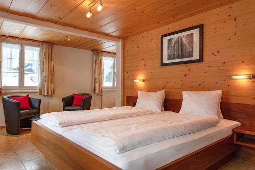 a bed in a wooden room with two chairs at Hotel Frohe Aussicht in Weissbad