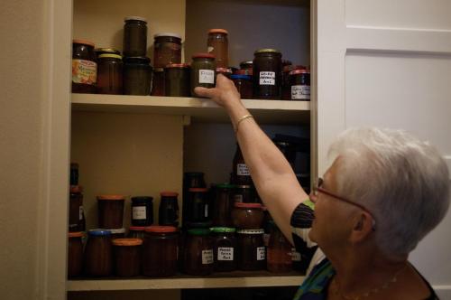 an older woman reaching for a bottle in a pantry at Hôtel Ladagnous in Peyrouse