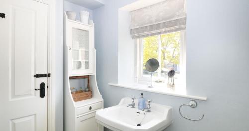 a white bathroom with a sink and a window at Unicorn Cottage in Bakewell