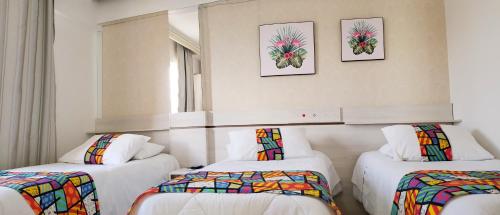 a room with three beds and two pictures on the wall at Capão da Canoa - Hotel Rediadri in Capão da Canoa