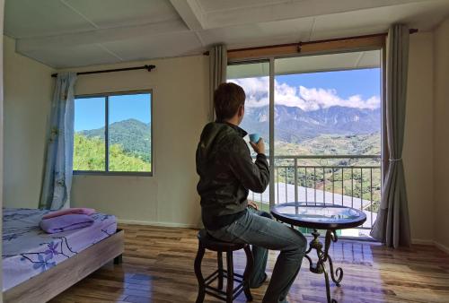 a person sitting on a stool looking out of a window at Nulu View Cabin in Kundasang