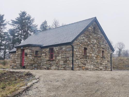 a stone building with red windows in a field at Glenkeel Cottage in Manorhamilton