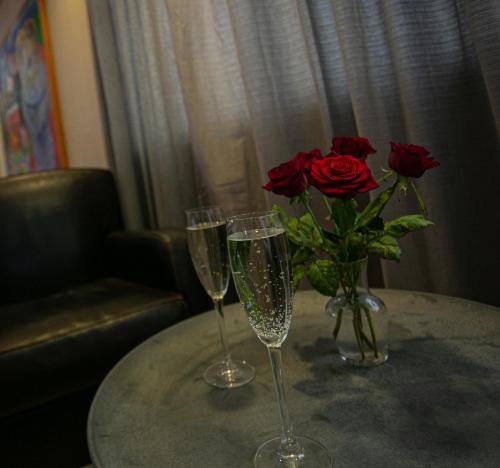 two wine glasses and a vase with roses on a table at Hotel Norðurland in Akureyri