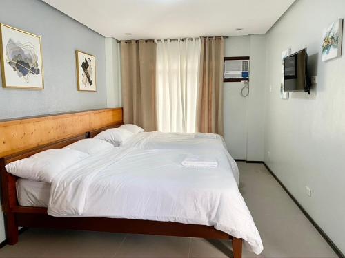 um quarto com uma cama com lençóis brancos e uma televisão em Philippa's Bed and Breakfast em Iloilo