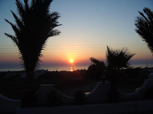 a sunset over the ocean with palm trees at Stavros Villas in Karterados