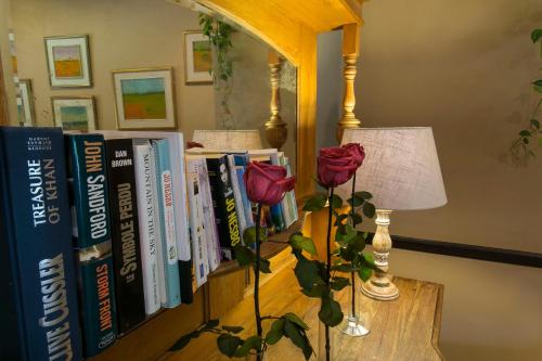 a book shelf with books and a rose on a table at Hlangana Lodge in Oudtshoorn