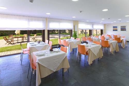 un restaurante con mesas blancas y sillas naranjas en Posada La Robla en La Cueva