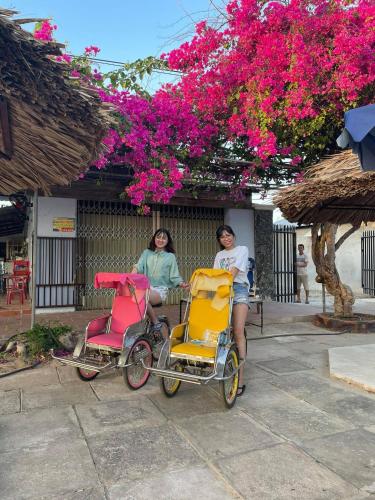 two women sitting in wheelchairs under a tree with pink flowers at Nhà nghỉ Cát Đằng Hồ Tràm in Ho Tram