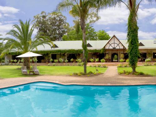 a resort with a swimming pool in front of a house at Hlangana Lodge in Oudtshoorn